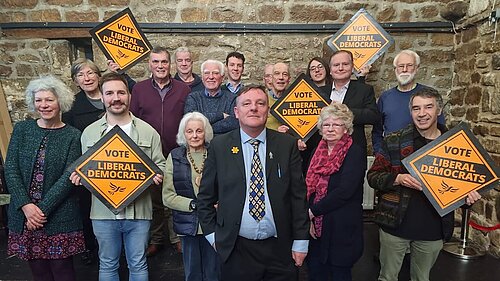 Header image of many Leeds North West members standing in a group with PPC Sandy Lay in the centre. Members are holding Liberal Democrat Diamonds.